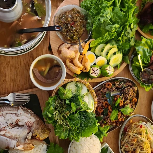 A vibrant Thai feast with soup, whole fish, papaya salad, and fresh vegetables on a wooden table.