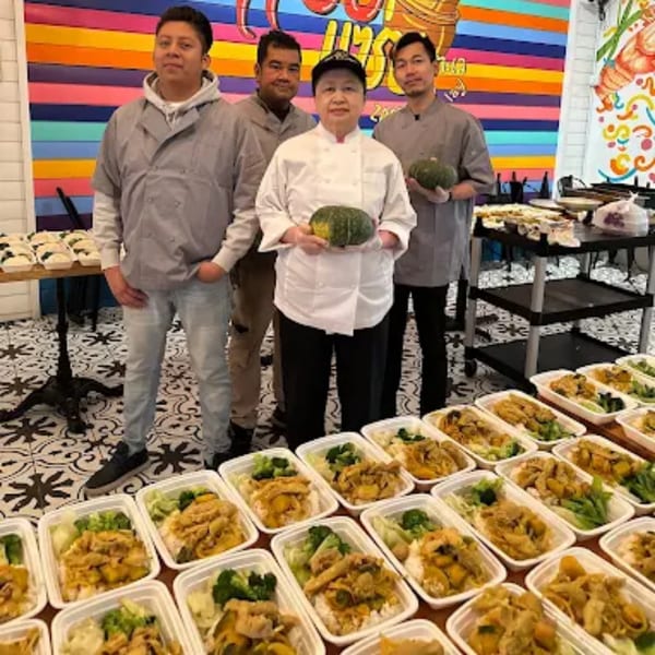 Four Zaab Zaab chefs stand proudly with prepared Thai meals in to-go containers and decorative gourds.