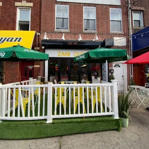 Zaab Zaab Thai restaurant exterior with outdoor dining area, green umbrellas, and yellow chairs.