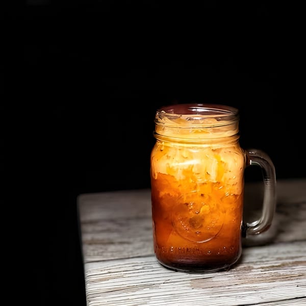 Zaab Zaab Thai iced tea in a mason jar with cream on a rustic wooden table.