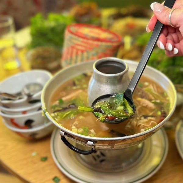 A hand spoons a serving of Zaab Zaab's Thai hot pot, filled with broth, vegetables, and meat.