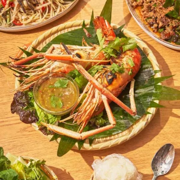 Grilled prawns with dipping sauce, cilantro, and banana leaves on a woven plate at Zaab Zaab.