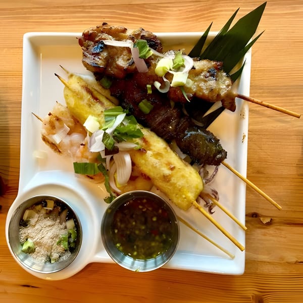 Zaab Zaab's grilled skewers, including shrimp, pork, and beef, with dipping sauces on a white plate.